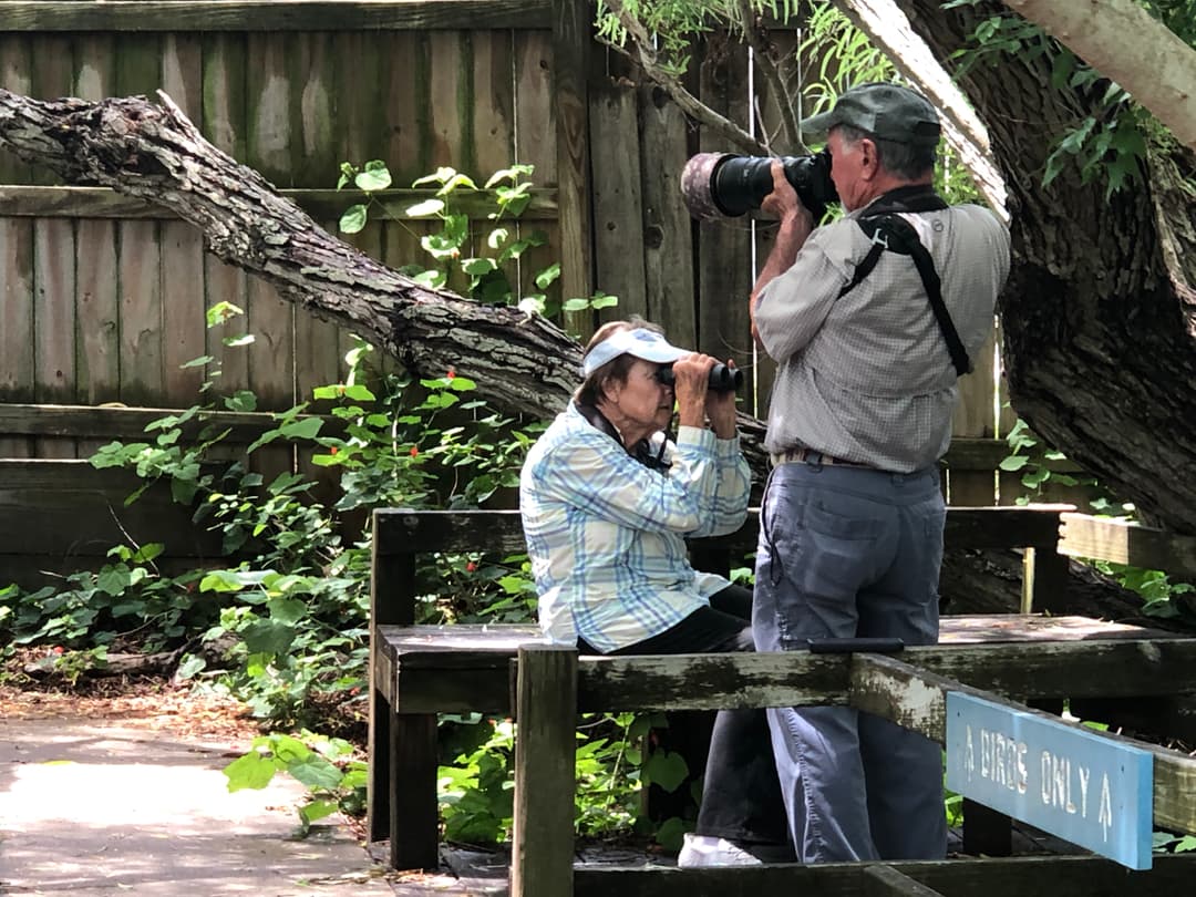 Birders with binoculars and telephoto lenses at Paradise Pond Port Aransas — Birds Only sign